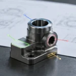 مكتب مراجعة هندسية يعرض جزءًا معدنيًا صغيرًا ورسمًا يُستخدم لتحديد ميزات CNC التي يجب أن تبقى مشغلة آليًا بعد التحويل إلى MIM.