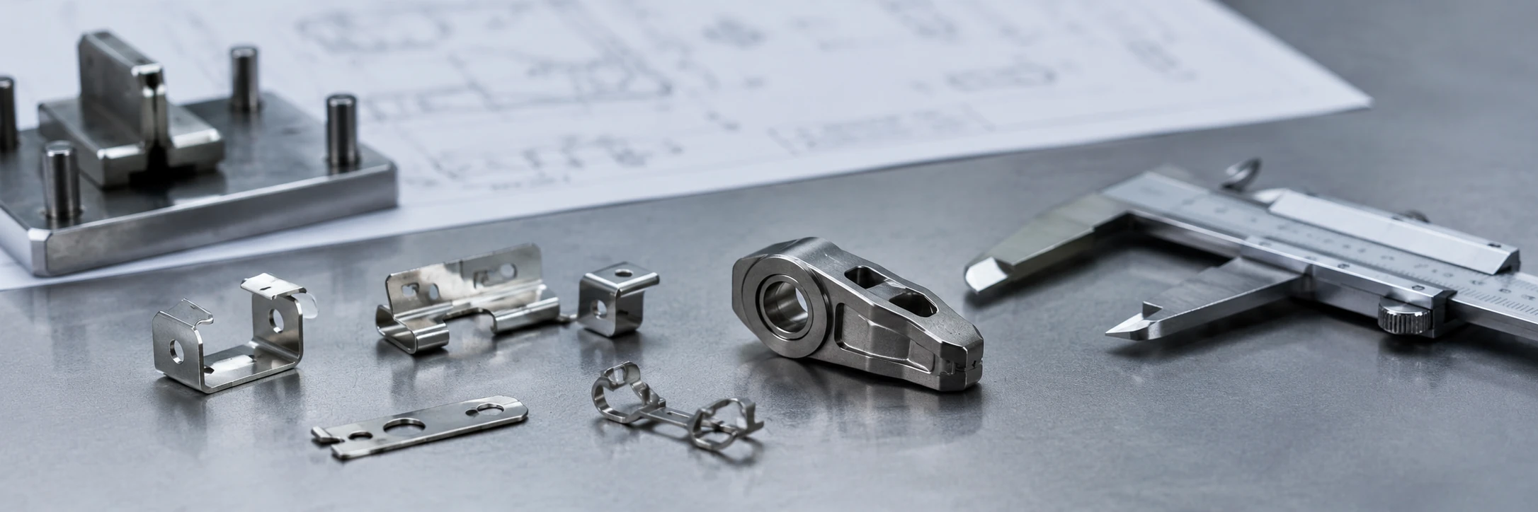 Engineering review desk showing small stamped assembly parts beside a compact one-piece MIM concept component for process selection review.