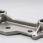 Compact sintered metal bracket with ribs, cored bosses, mounting holes and stable datum faces on an inspection bench